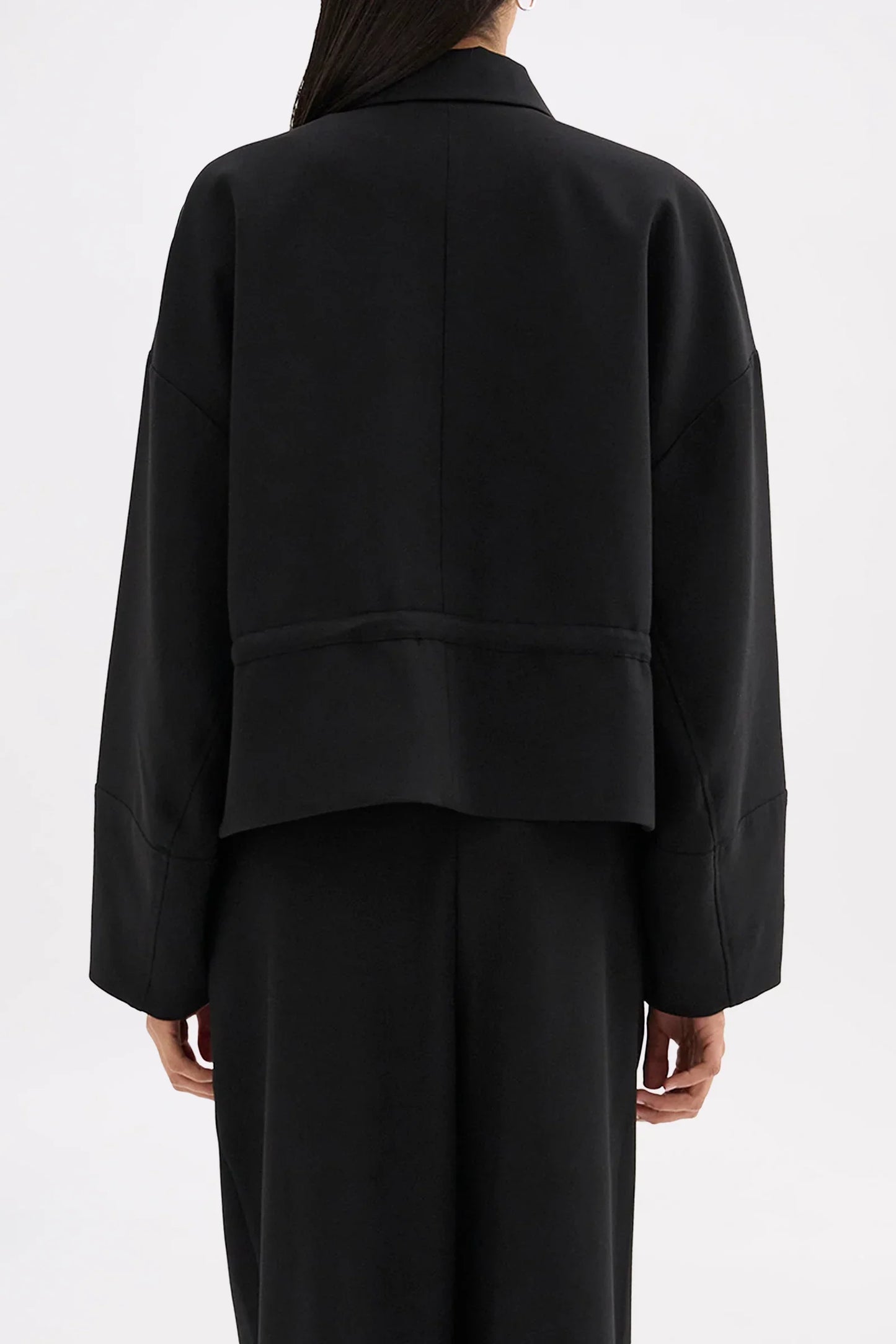 Back view of a woman wearing an oversized black cropped blazer and matching black trousers.