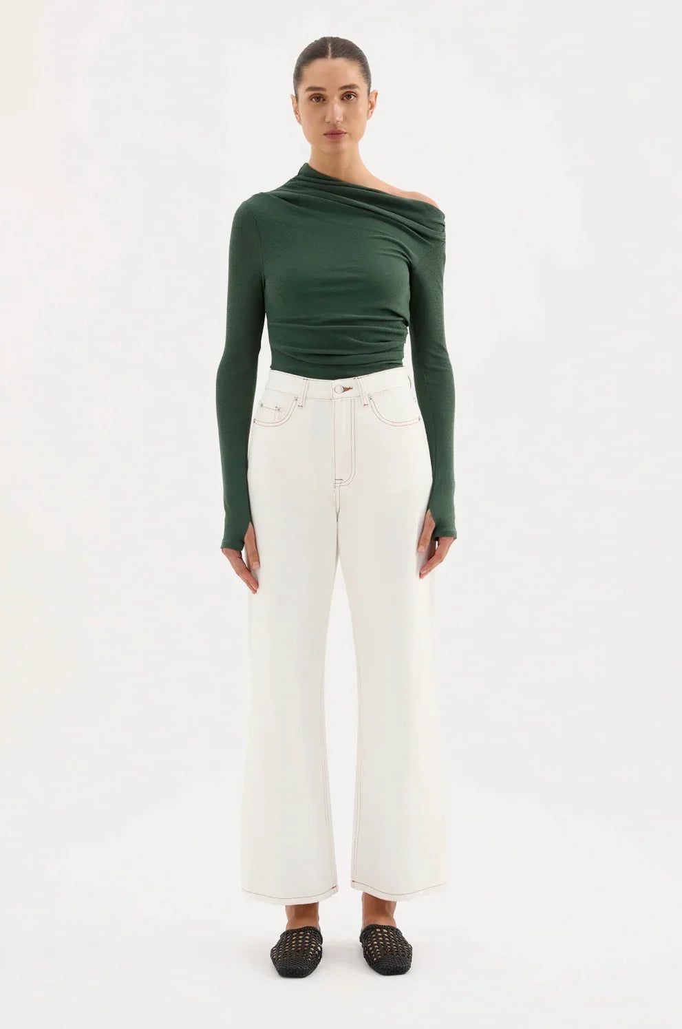 Woman wearing green one-shoulder top, white high-waisted wide-leg jeans, black flats