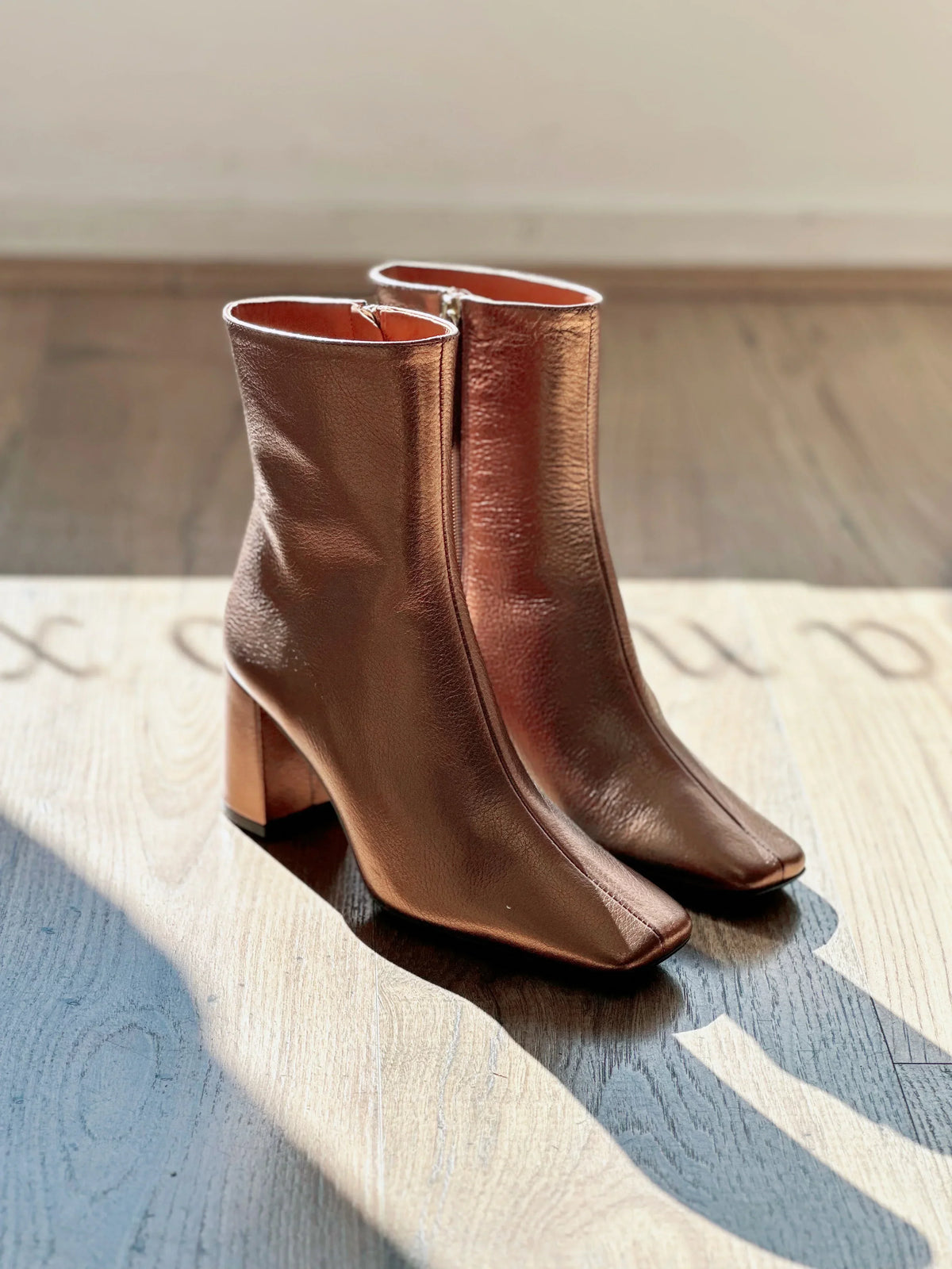 NEO Galaxy Copper Boots featuring a metallic copper finish and block heel on a wooden surface.