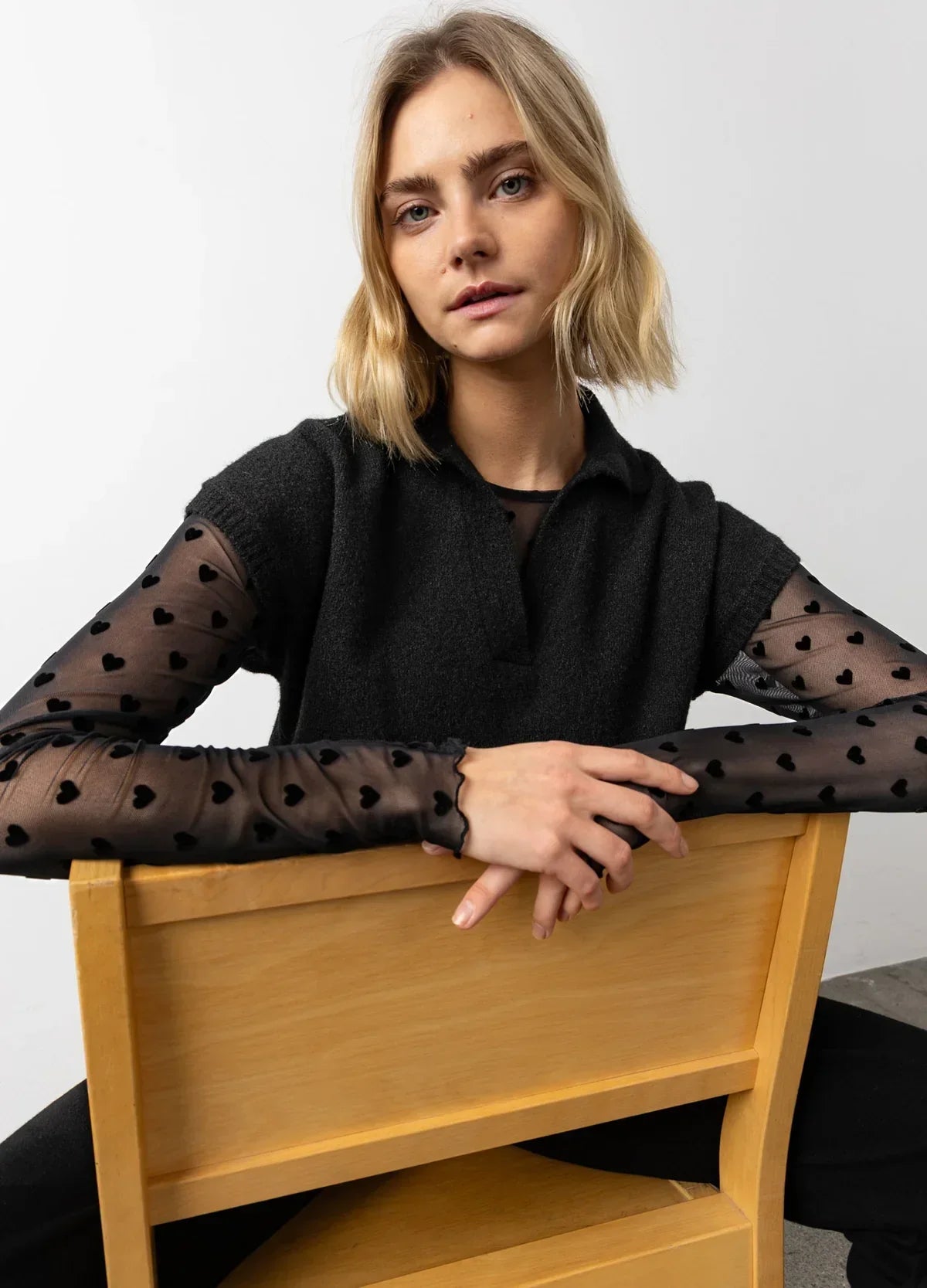 Woman in black short-sleeve knit top over sheer black mesh sleeves with heart pattern