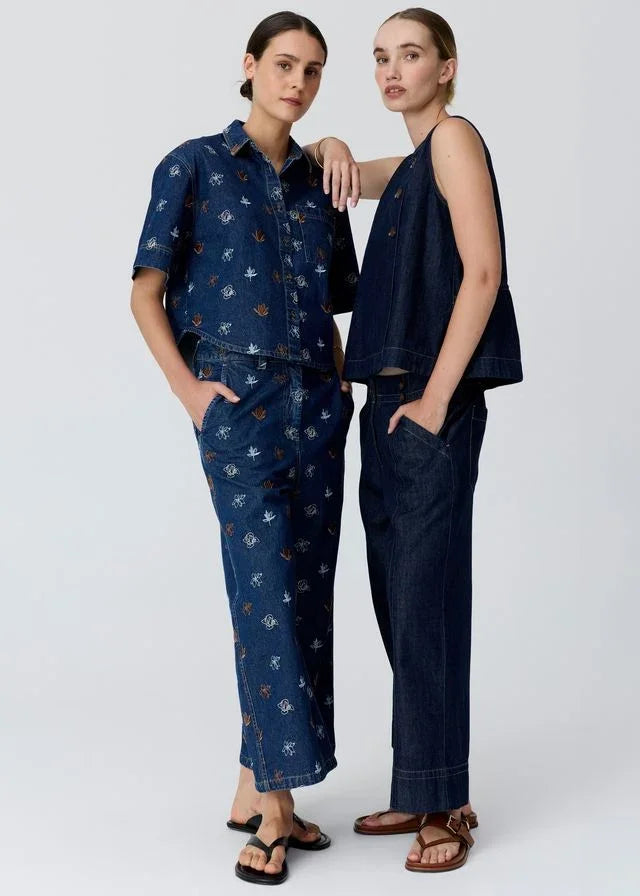 Two women in stylish denim outfits, one with floral print shirt and pants, other in sleeveless top and wide-leg jeans