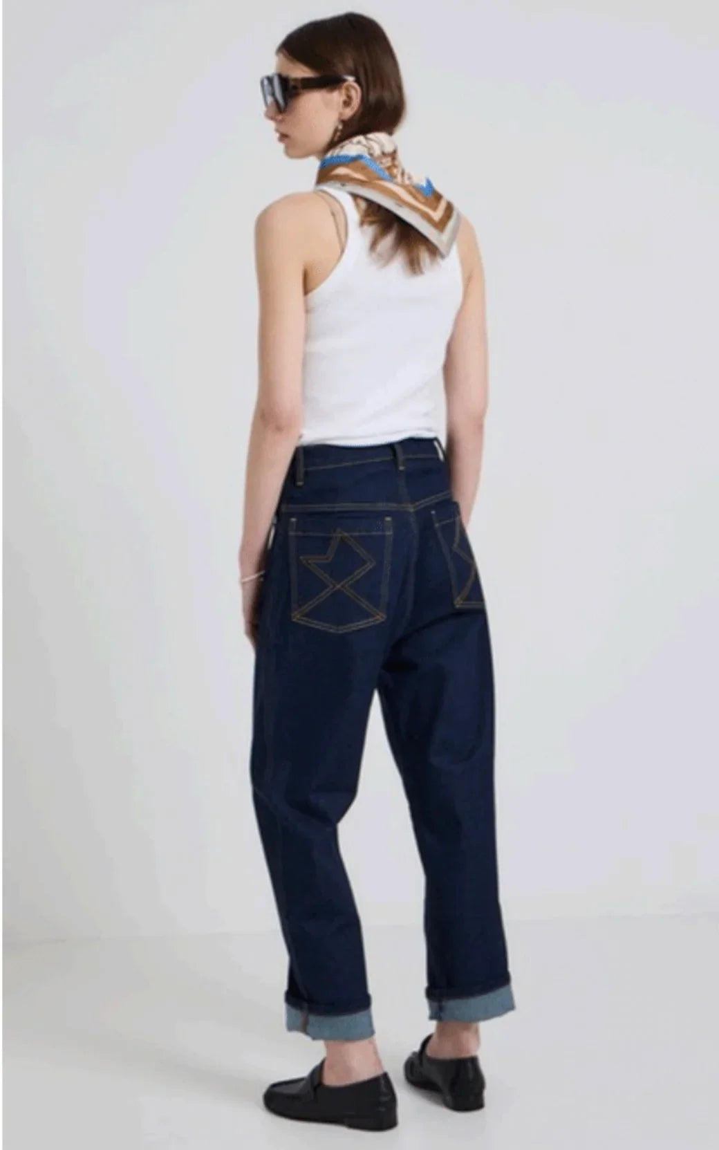Woman wearing a white tank top, dark wash wide-leg jeans, and a patterned neck scarf.