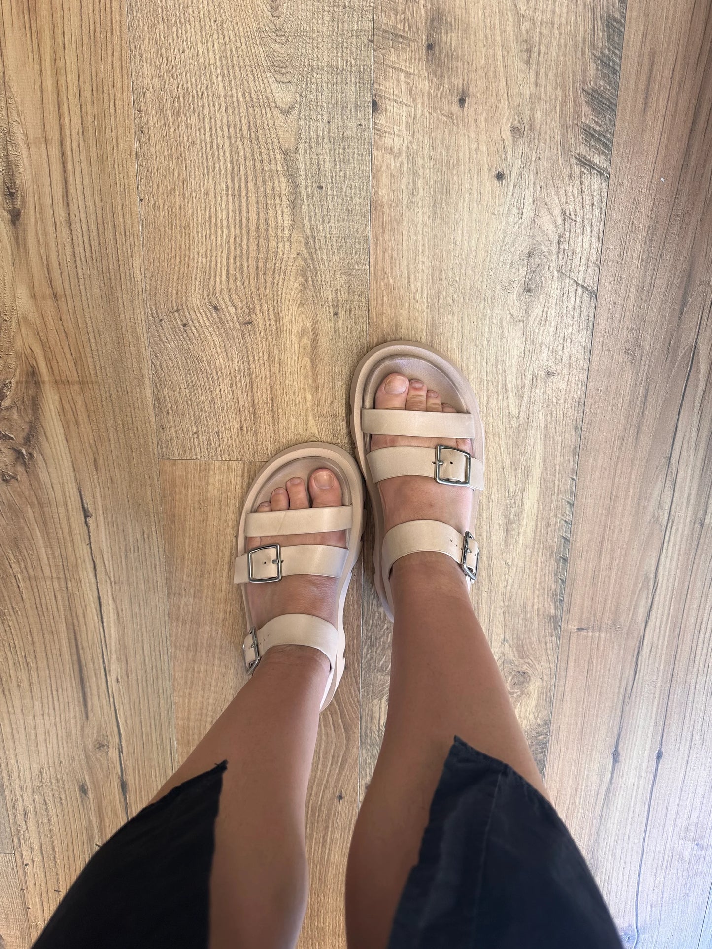 Beige strappy sandals with buckles on wooden floor, women's summer footwear