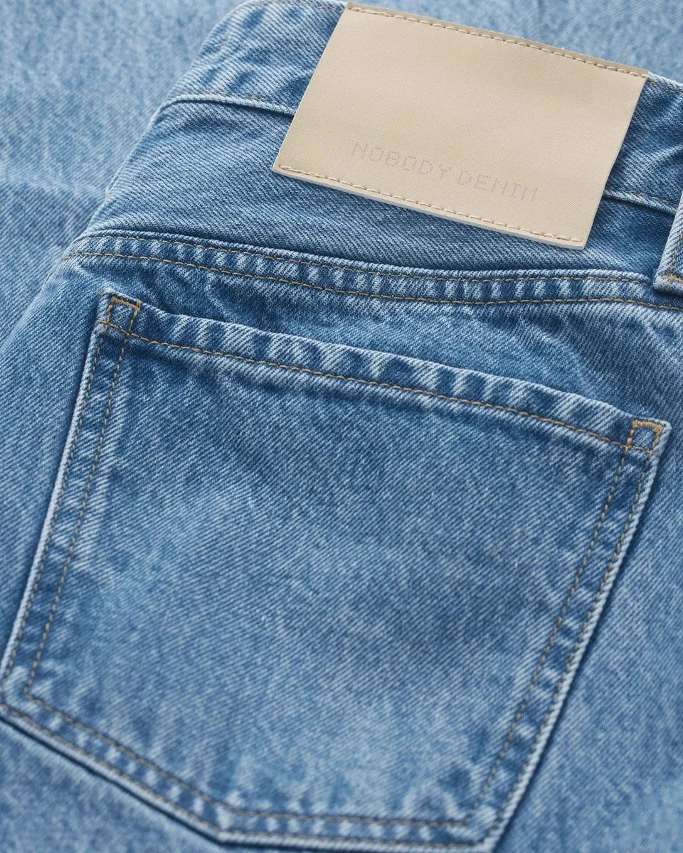 Close-up of blue denim jeans back pocket with tan leather patch, women's fashion