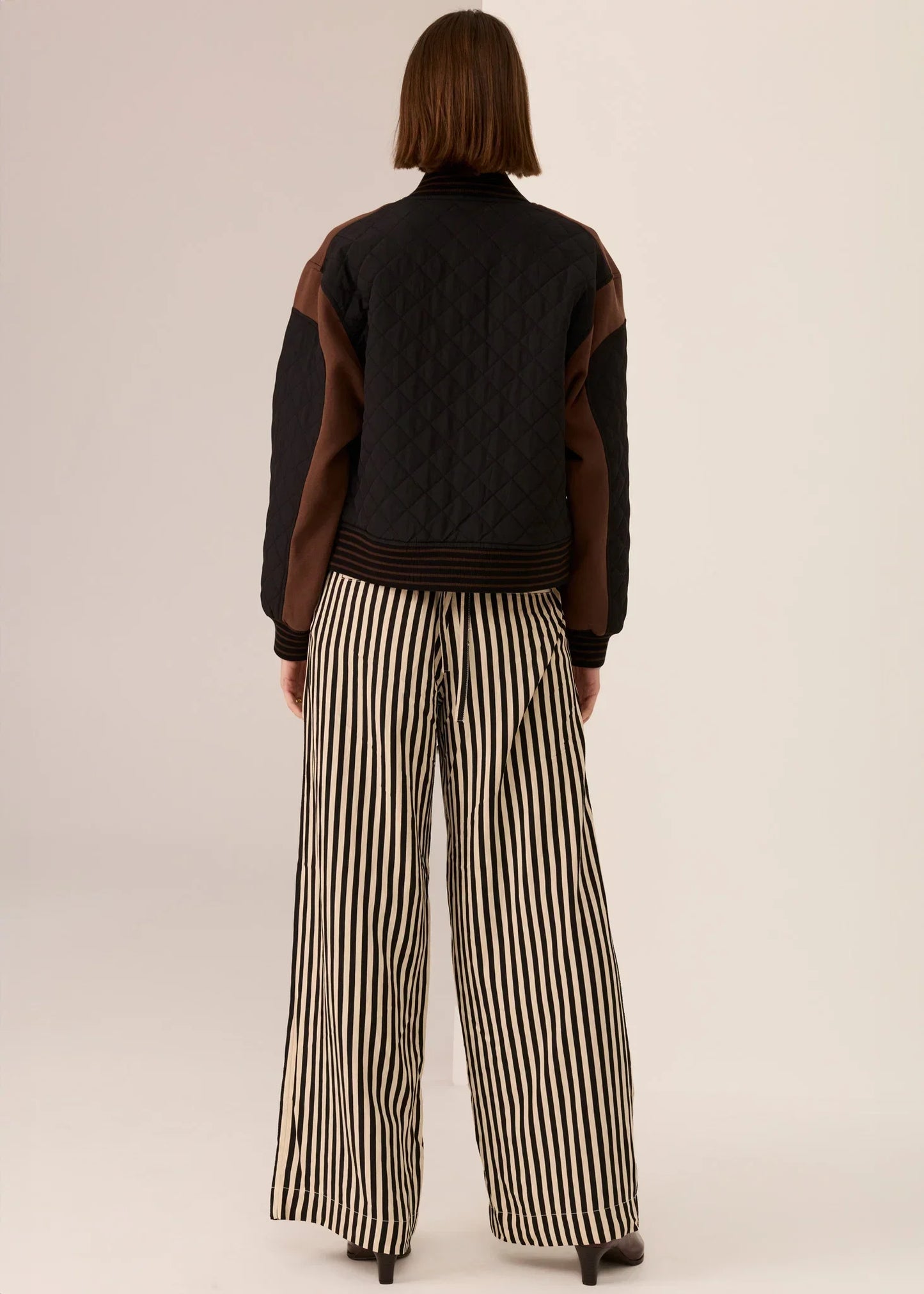 Black quilted jacket with brown sleeves paired with black and cream striped wide-leg pants