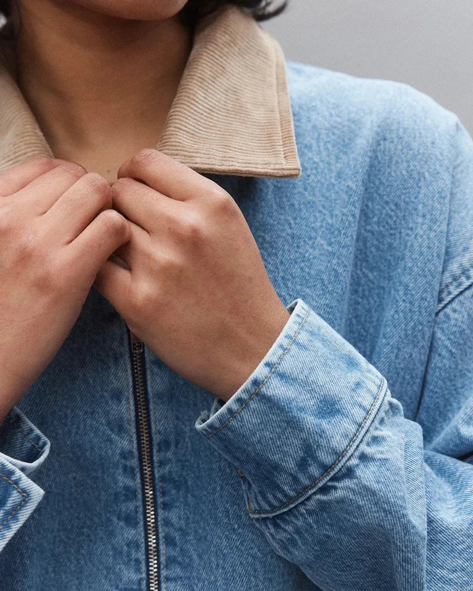 Woman adjusting blue denim jacket with beige corduroy collar, close-up fashion detail