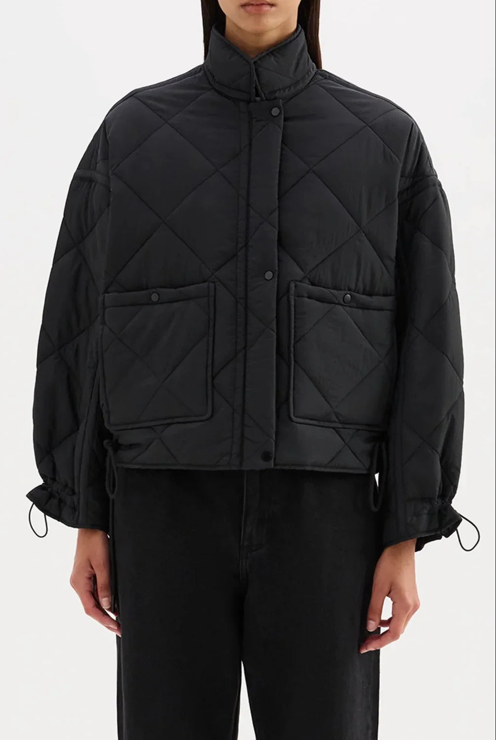 Black quilted puffer jacket with front pockets and drawstring cuffs, styled with black pants