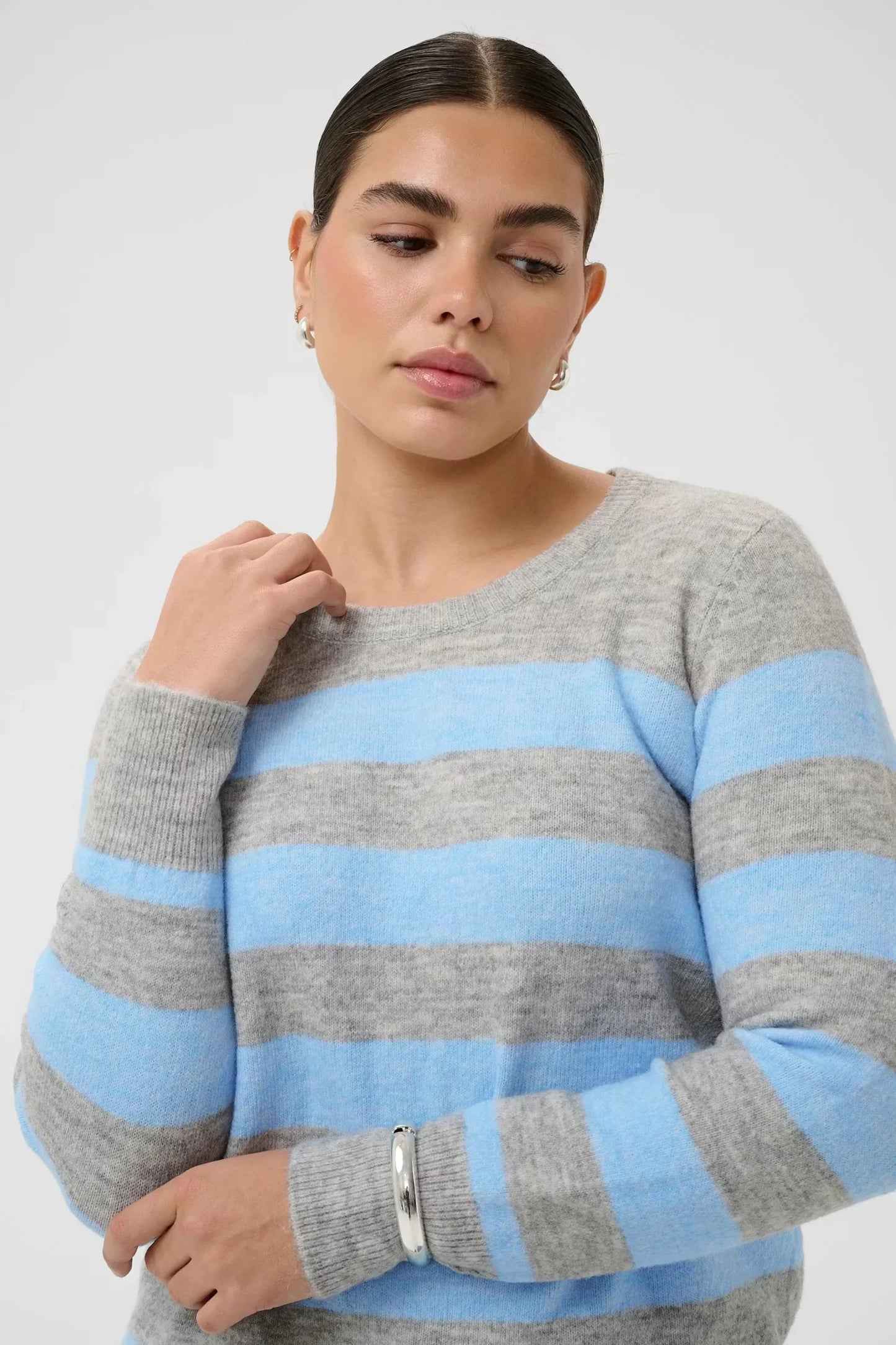 Gray and blue striped sweater with long sleeves, worn by a woman with silver accessories