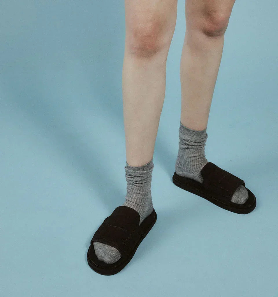 Black slide sandals with gray socks, women's casual footwear on blue background