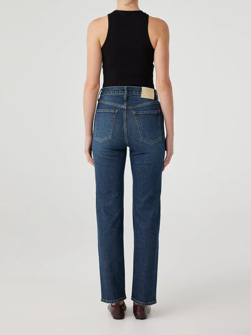Woman wearing dark wash straight-leg jeans with back pockets, paired with black ribbed top and brown shoes