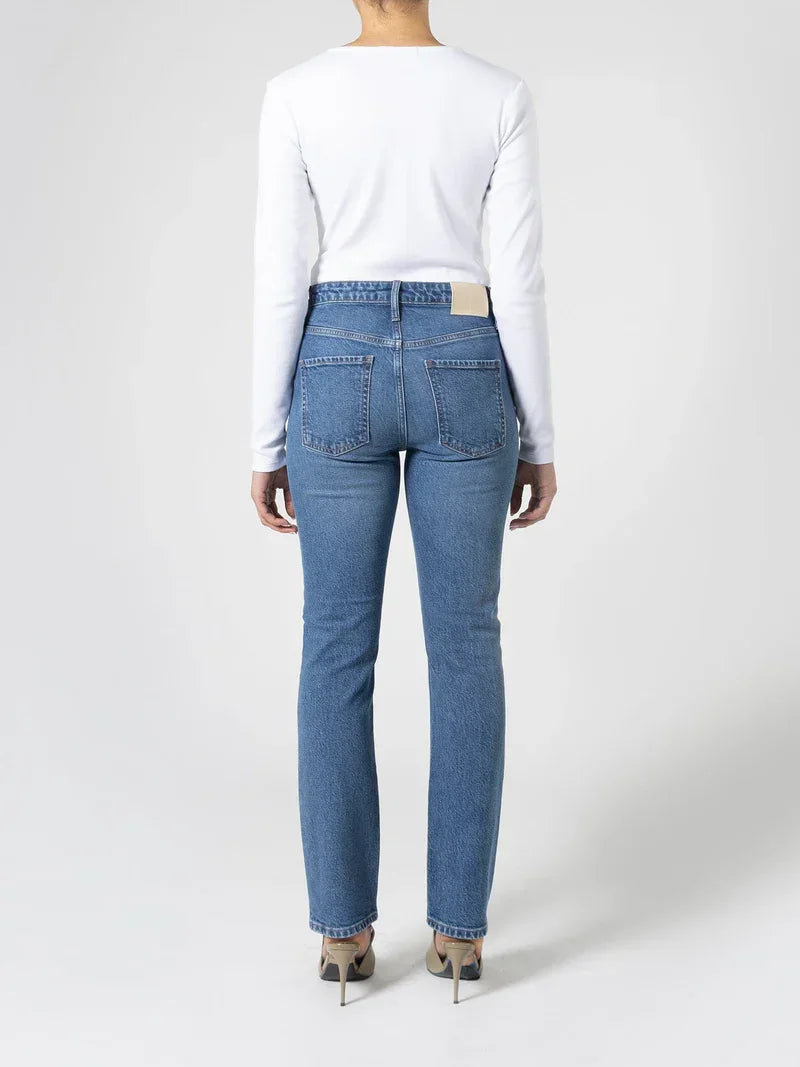 Women's blue denim jeans with straight leg cut, paired with white long sleeve top and heels