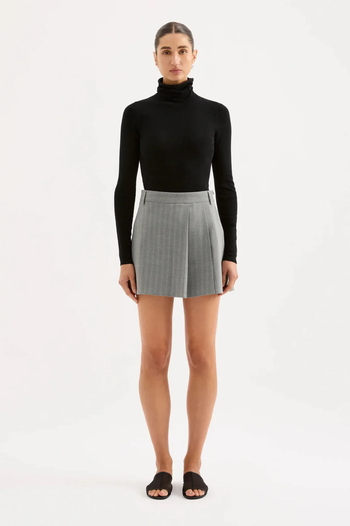 Woman wearing black turtleneck with grey pleated mini skirt and black sandals, women's fashion