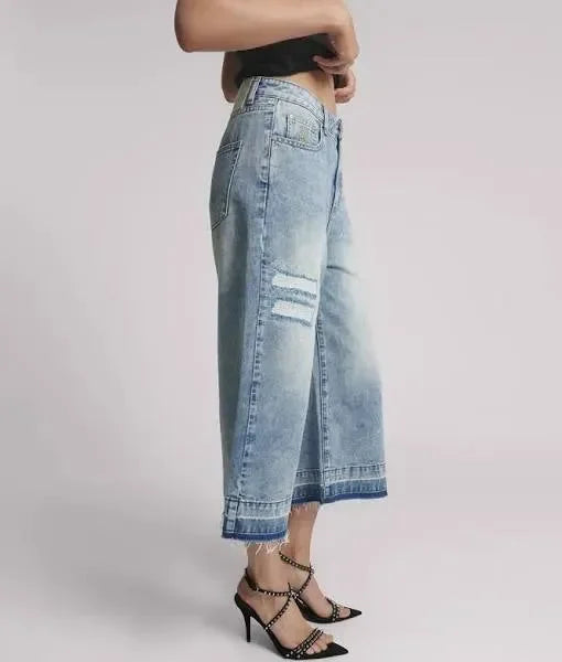 Light wash wide-leg cropped jeans with distressed details and frayed hems, styled with black strappy heels.