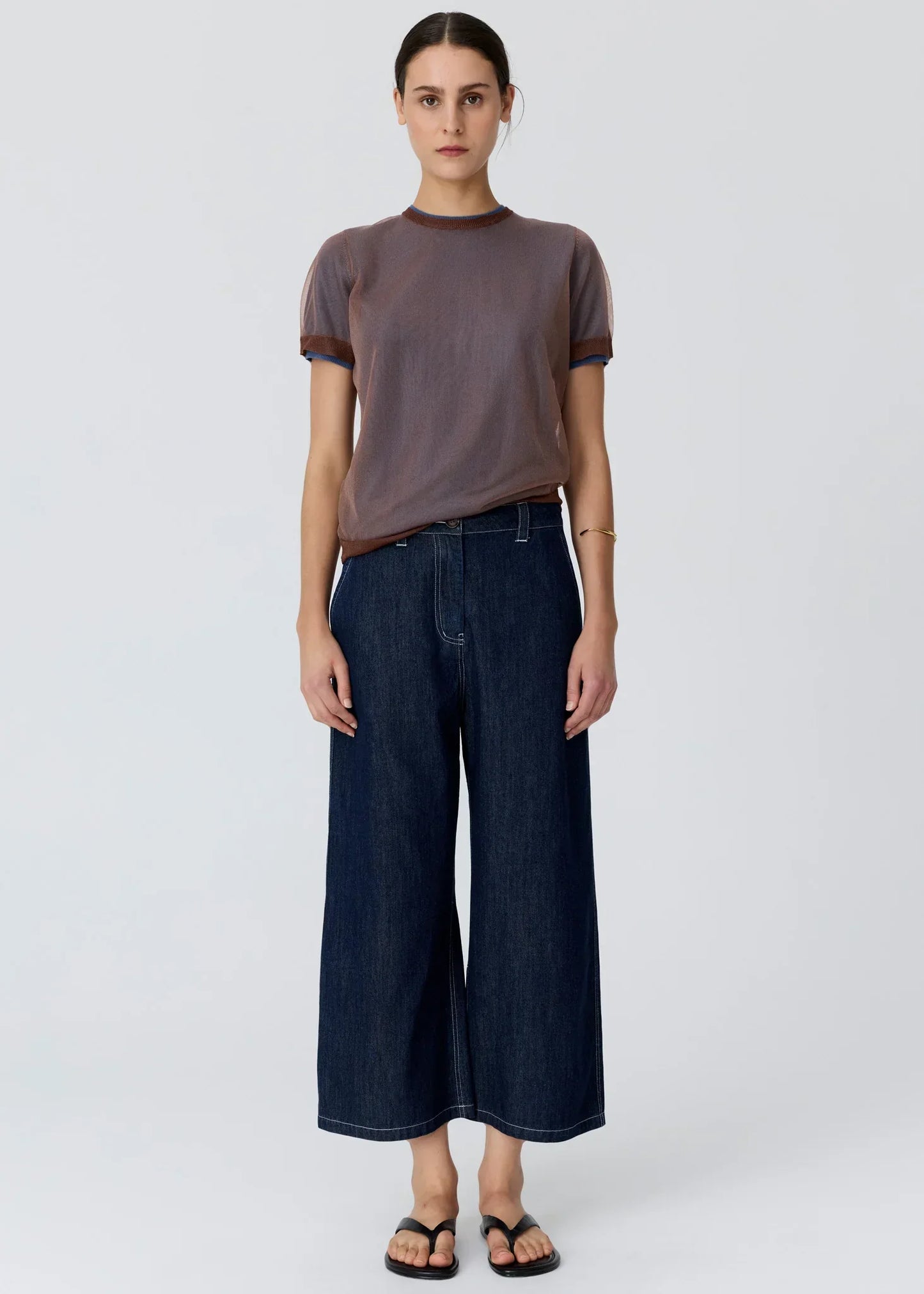 Woman wearing a sheer brown t-shirt and wide-leg dark wash denim trousers.