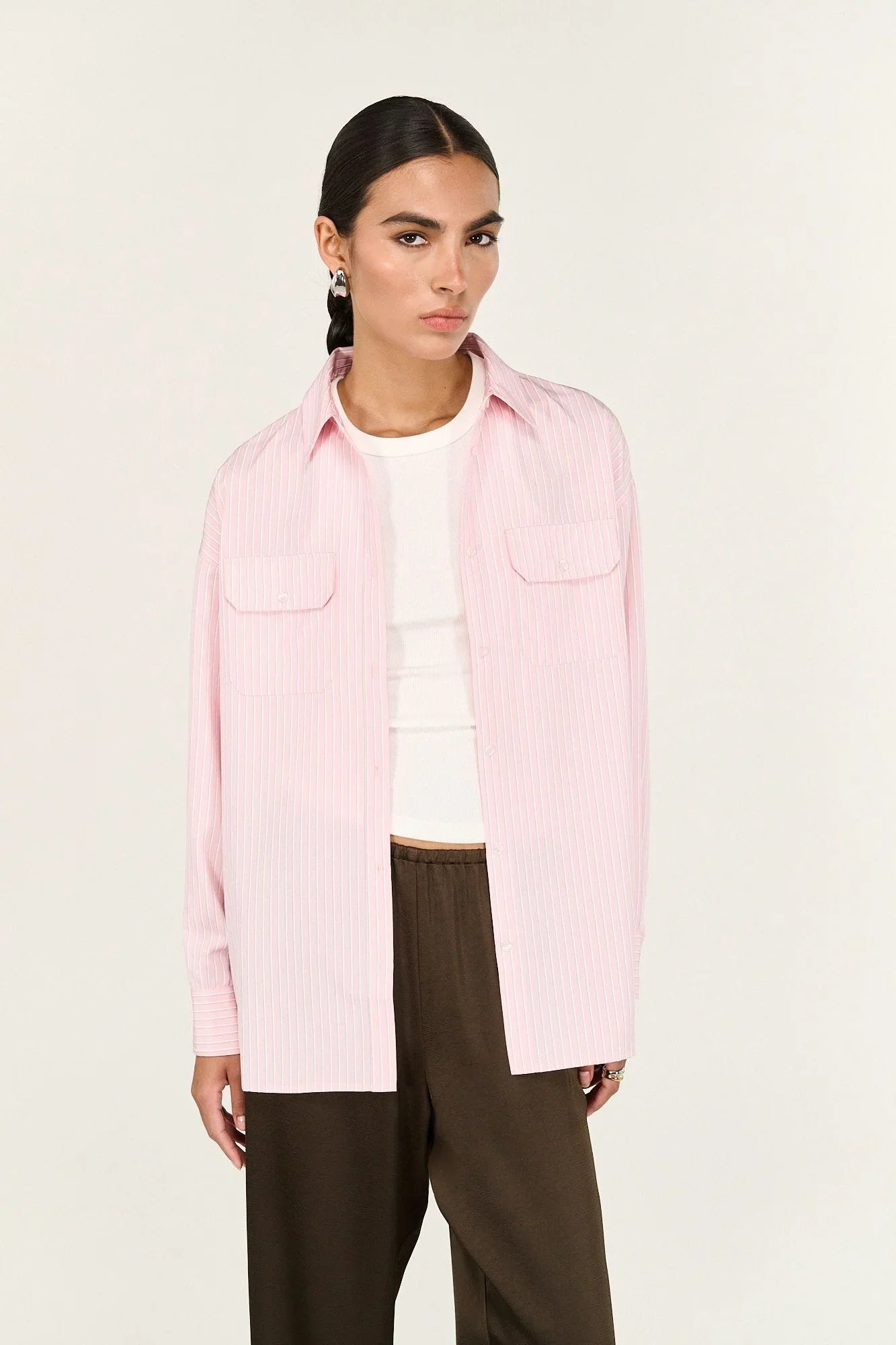 Woman in pink striped button-up shirt, white tank top, and brown pants, fashion studio shot