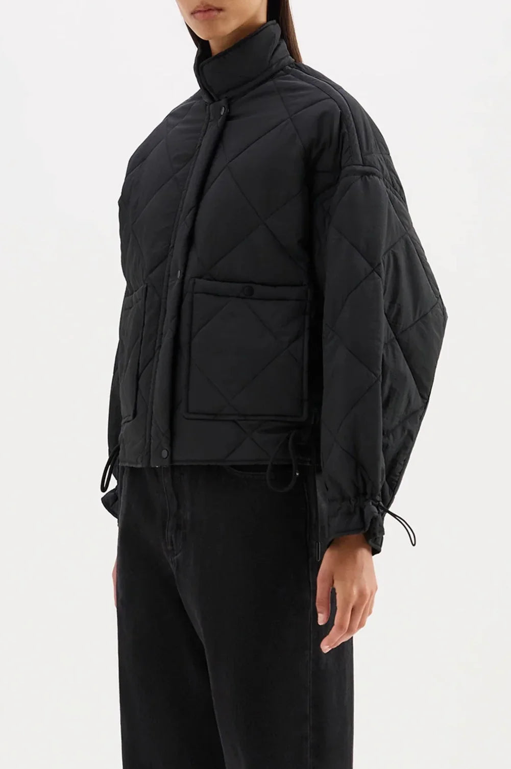 Black quilted puffer jacket with drawstring waist and front pockets, styled with black jeans