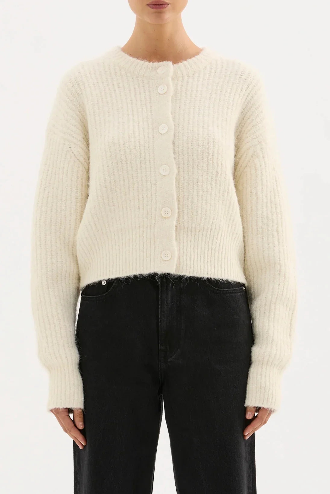 Woman wearing a cream ribbed knit cardigan with front buttons and black high-waisted jeans