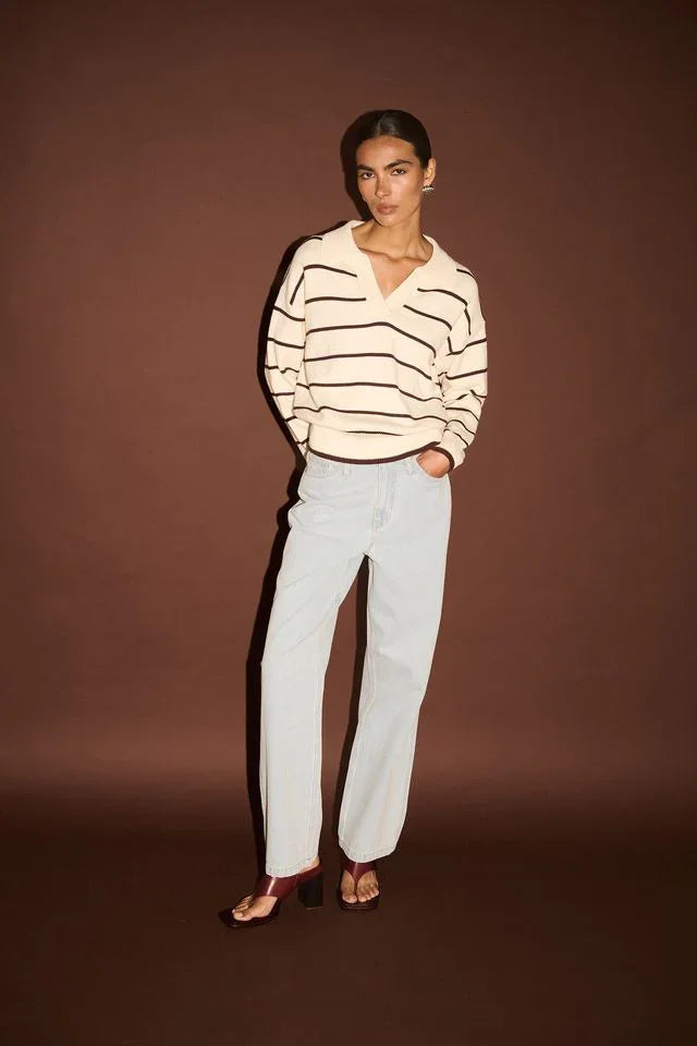 Woman in striped V-neck sweater, light wash jeans, and burgundy block heels, studio fashion shot