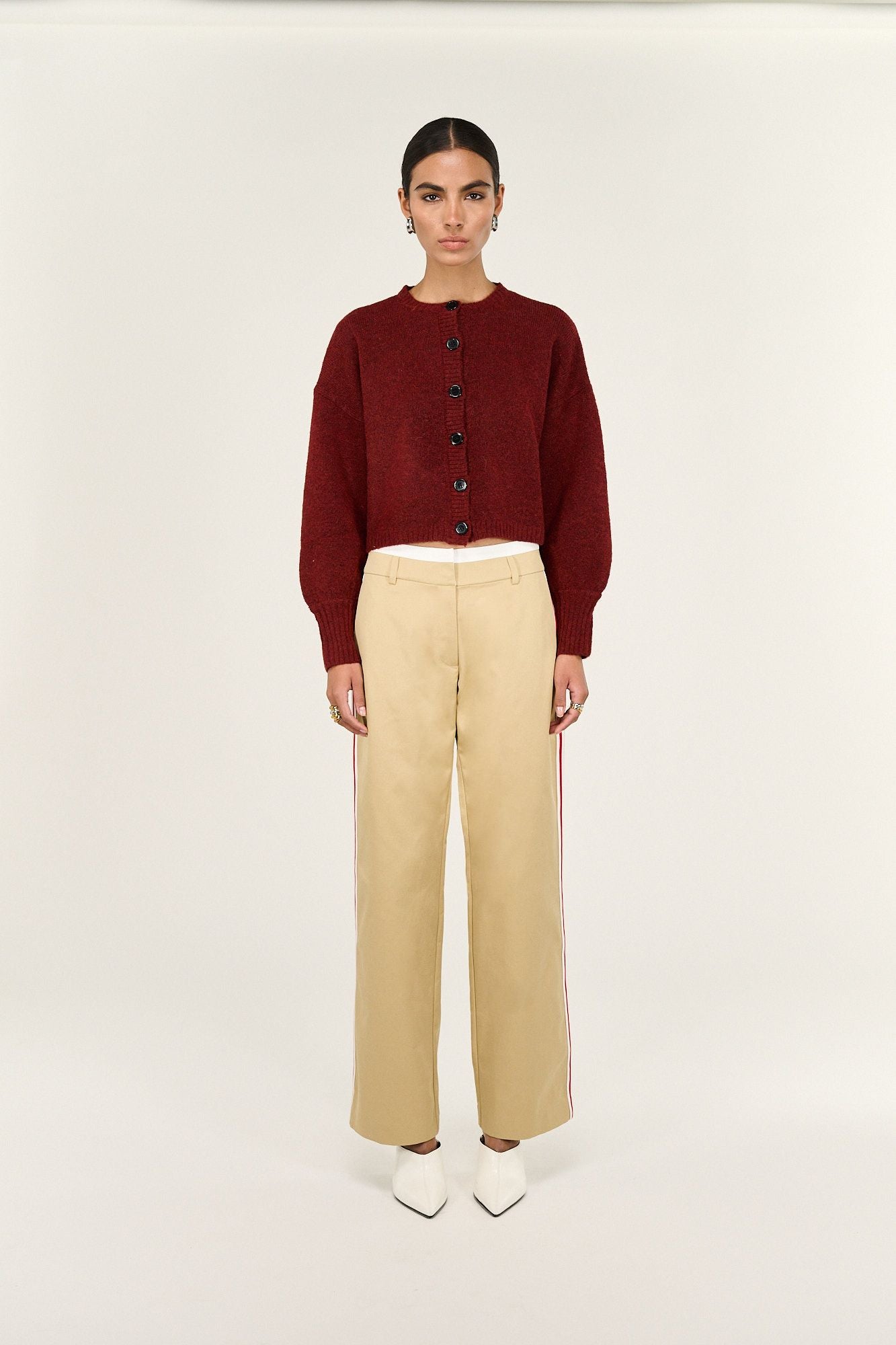 Woman wearing a burgundy button-up cardigan, beige wide-leg pants, and white heels