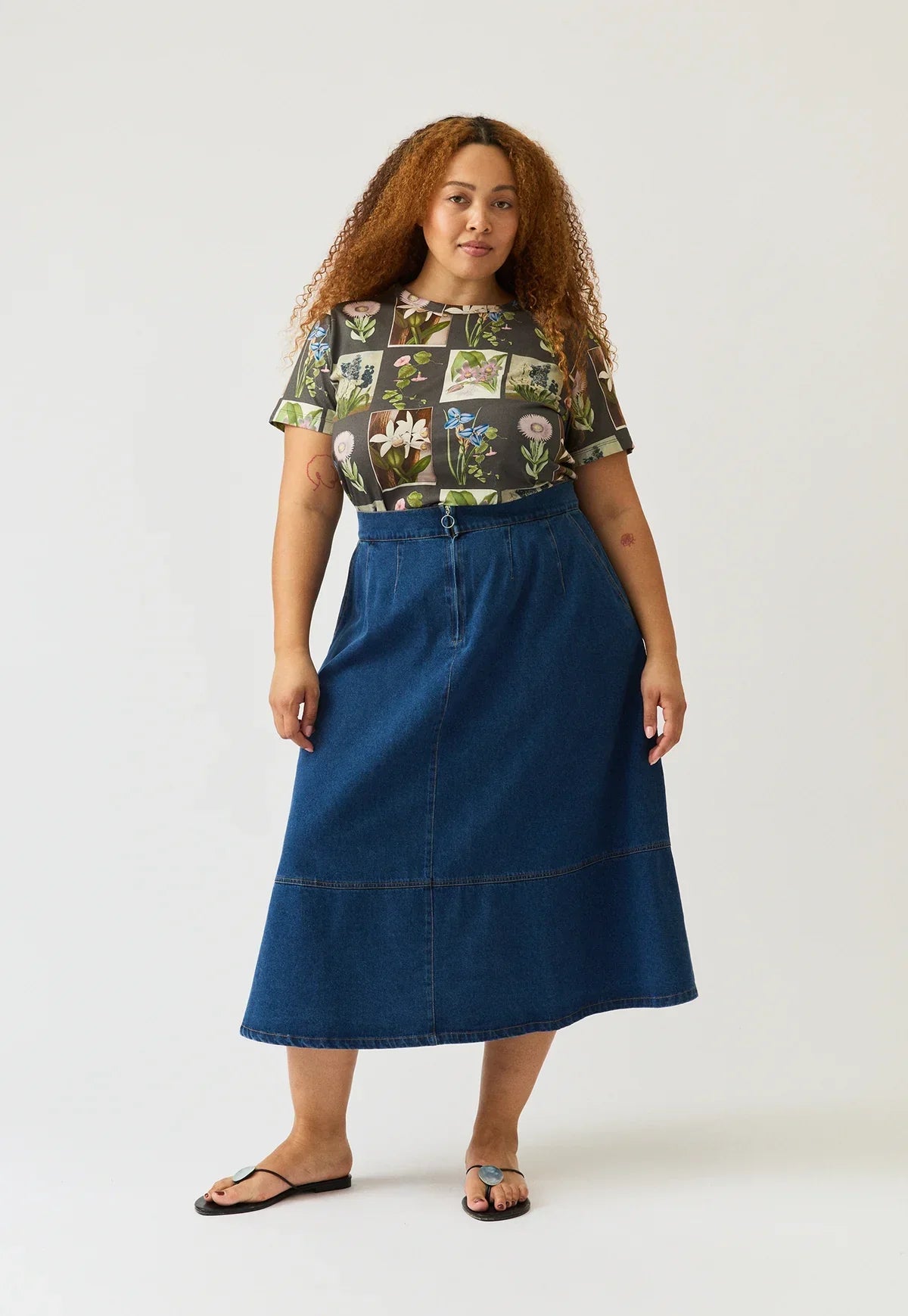 Woman wearing the NANCYBIRD Aries Denim Skirt in dark wash and a floral print t-shirt.