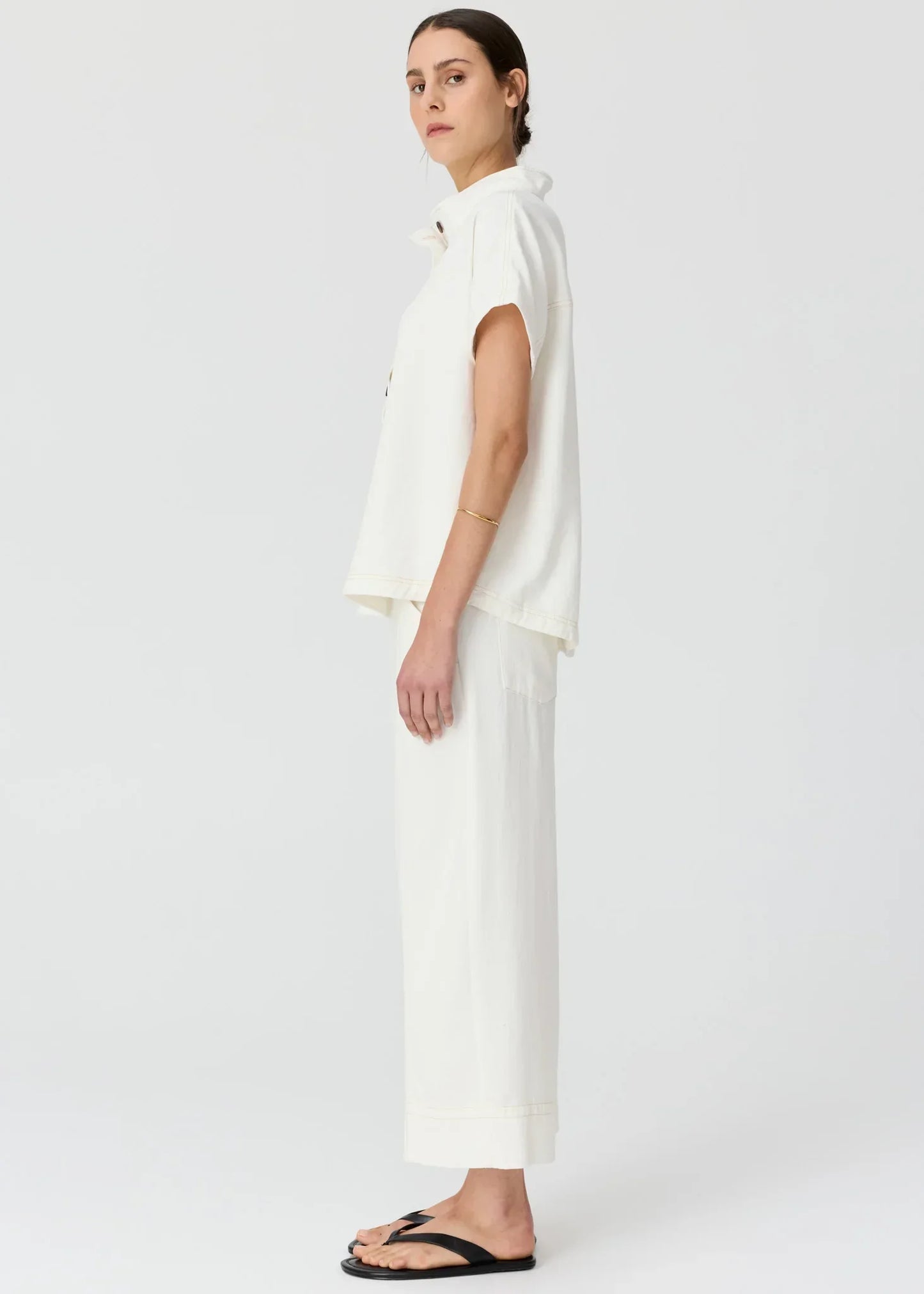 Woman in a white short-sleeved collared shirt and matching wide-leg trousers with black sandals.