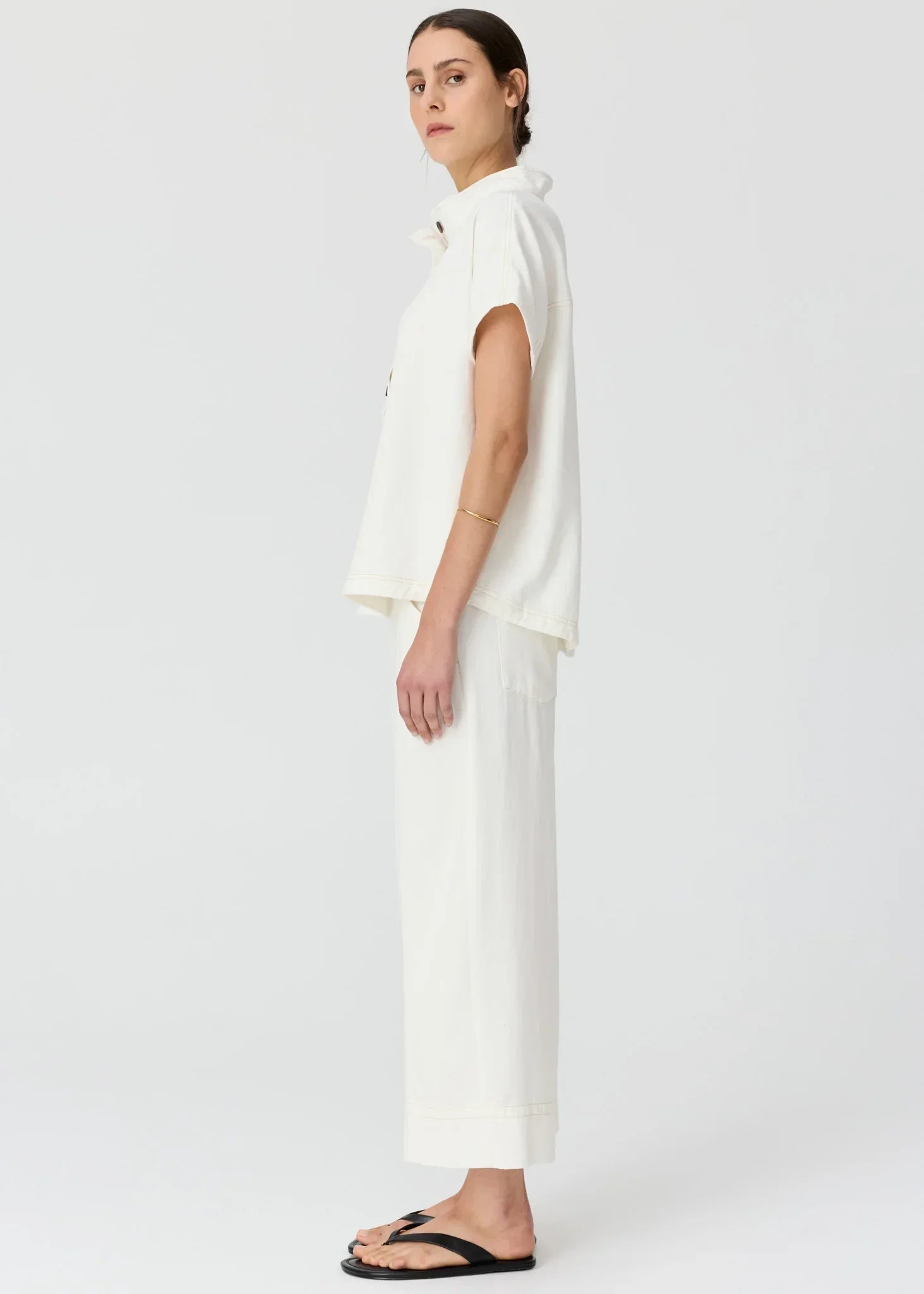 Woman in a white short-sleeved collared shirt and matching wide-leg trousers with black sandals.