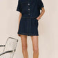 Woman in dark denim short-sleeve shirt and skirt set, beige sandals, and sunglasses at The Tartan Fox