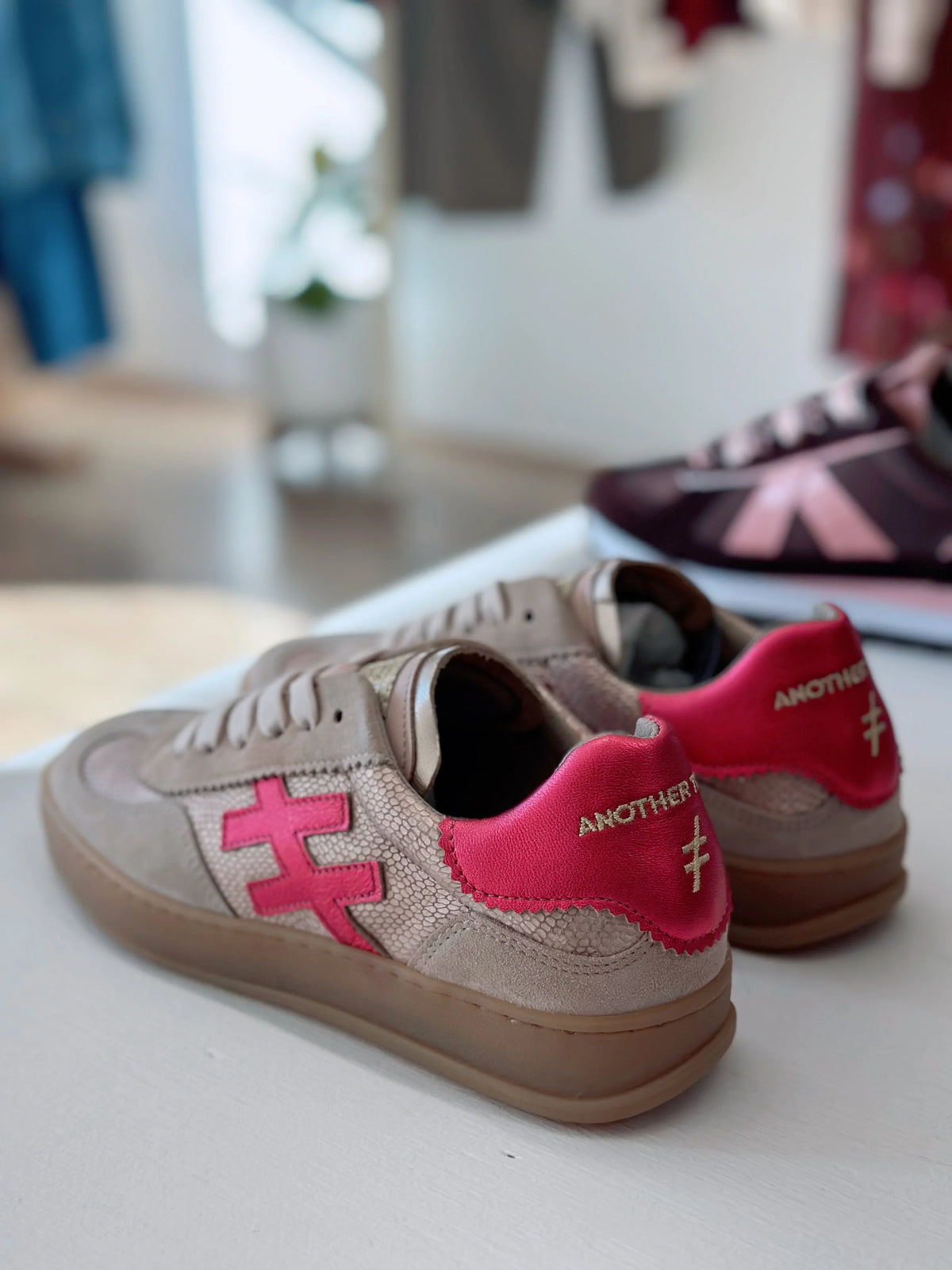 Pair of beige Another Tomorrow sneakers with pink logo accents on a white surface