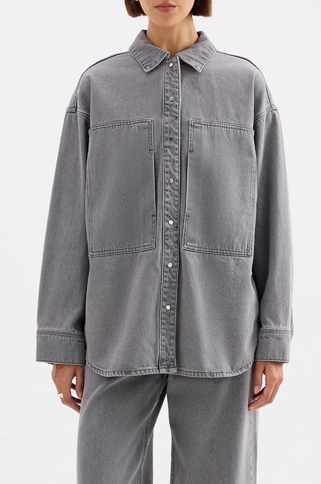 Woman wearing oversized grey denim shirt jacket with large front pockets and snap buttons