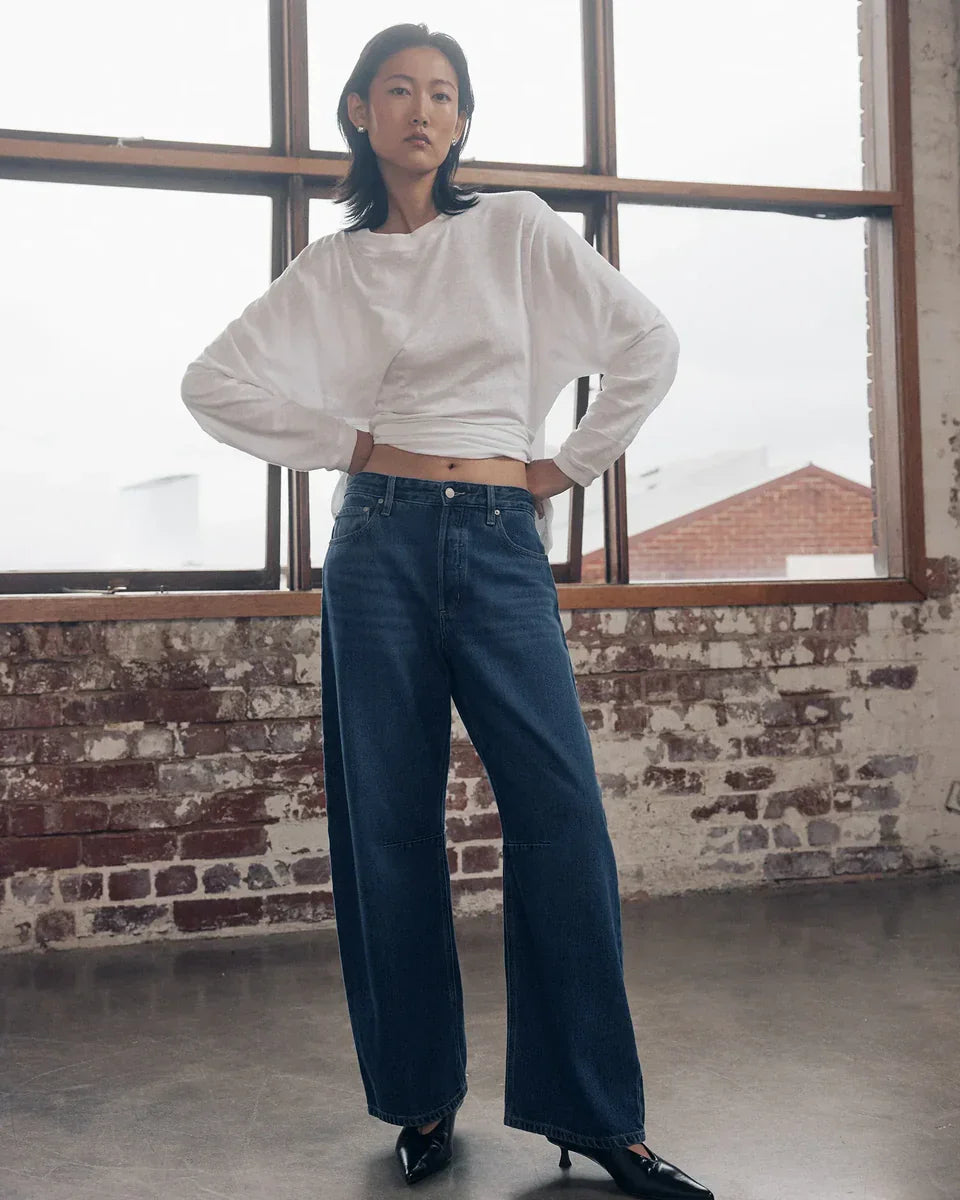 Woman in white long sleeve top and wide leg denim jeans, styled with black heels in loft setting