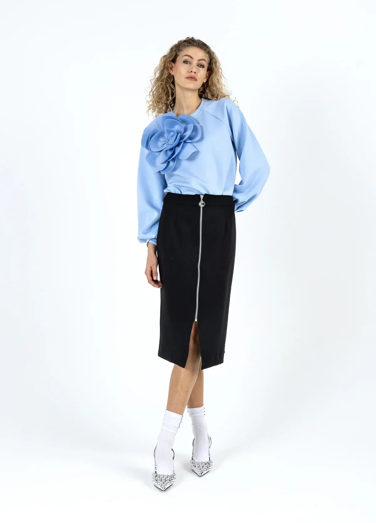 Woman in a blue blouse with large flower detail, black zip-front pencil skirt, and pointed heels