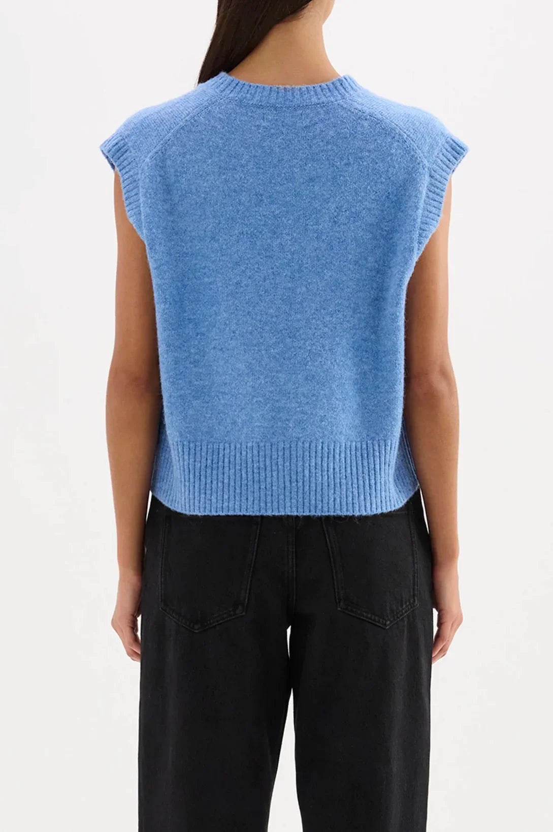 Back view of woman wearing blue sleeveless knit sweater vest and black high-waisted jeans