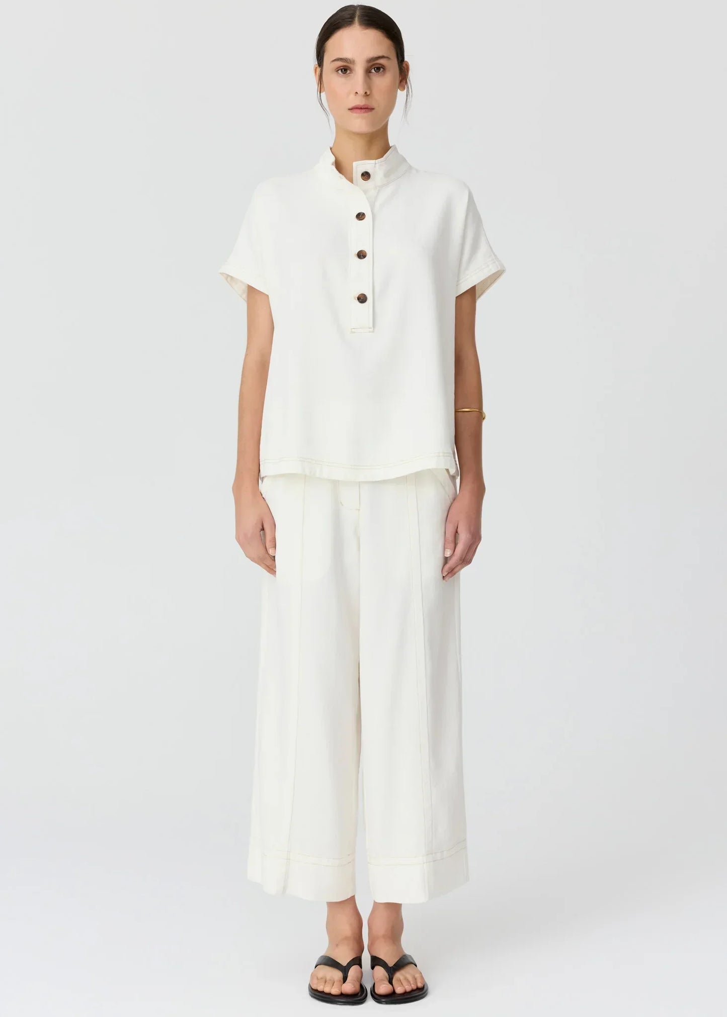 Woman wearing a white short-sleeve button-up top and matching wide-leg trousers.