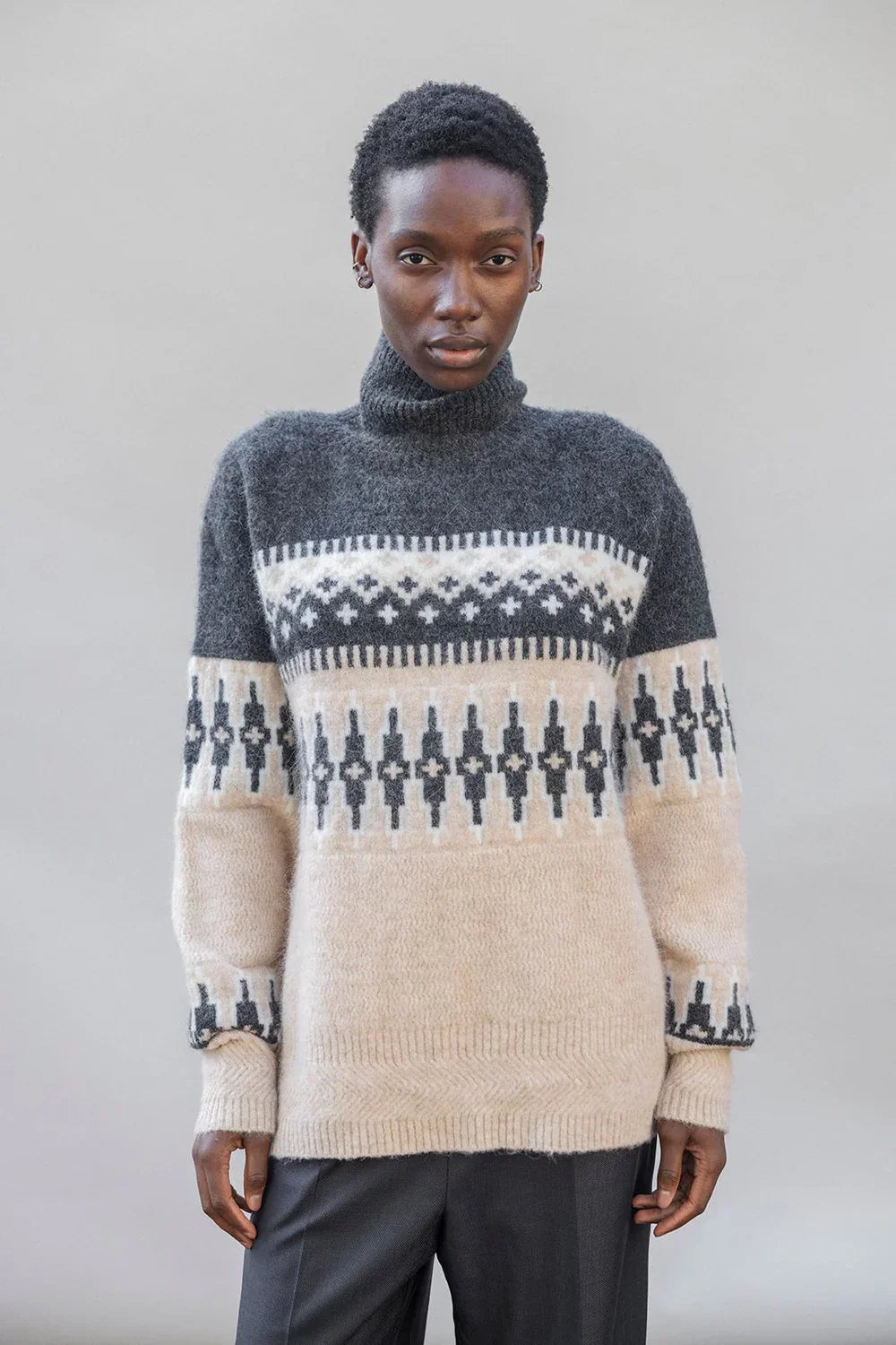 Woman wearing a cozy patterned turtleneck sweater in grey and beige with geometric knit design