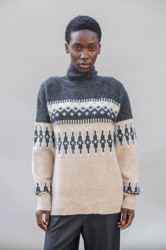 Woman wearing a cozy patterned turtleneck sweater in grey and beige with geometric knit design
