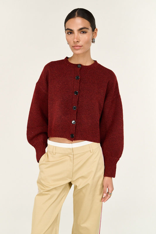 Woman wearing a cropped burgundy knit cardigan with black buttons and beige high-waisted pants.