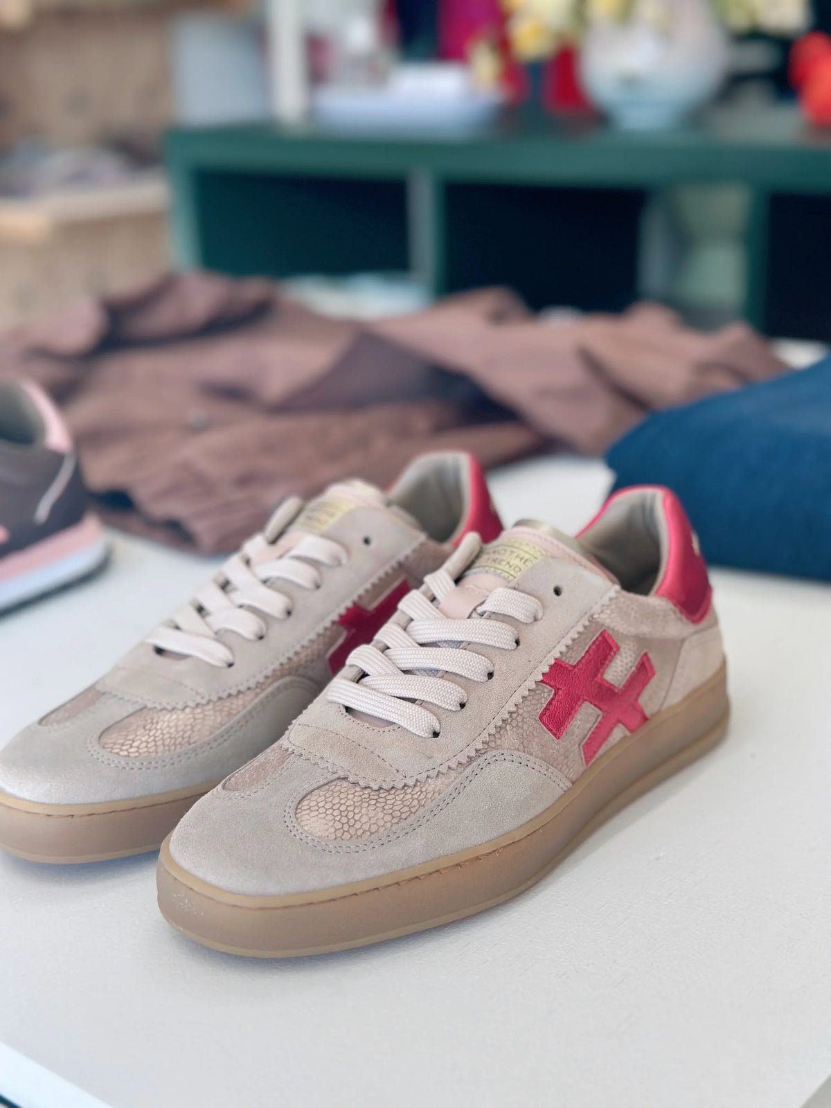 Pair of beige suede sneakers with red cross logos and snakeskin detail on a white surface
