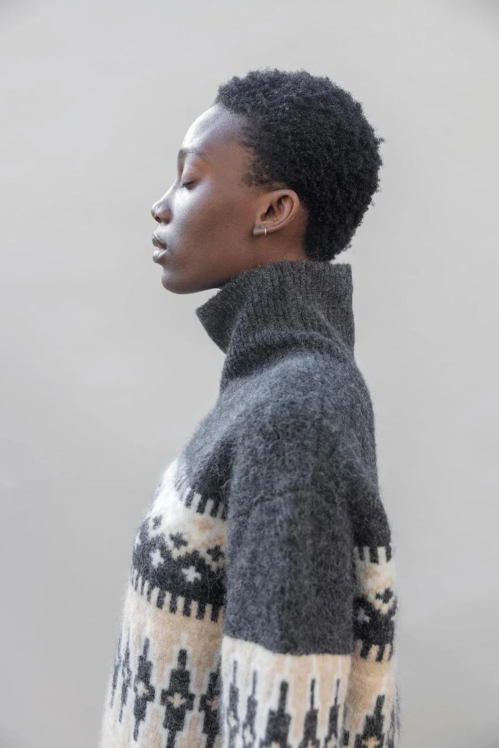 Side view of person wearing a high-neck, patterned wool sweater in grey and cream