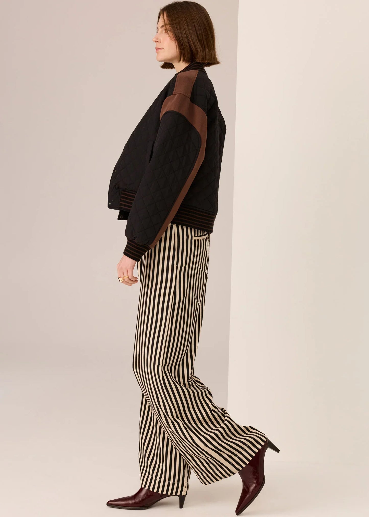 Woman in black quilted jacket, striped wide-leg pants, and burgundy heels