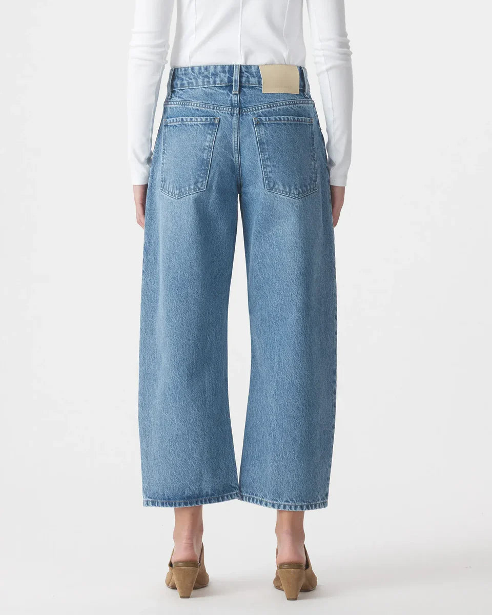 Back view of woman in high-waisted wide leg blue jeans and tan heels on white background