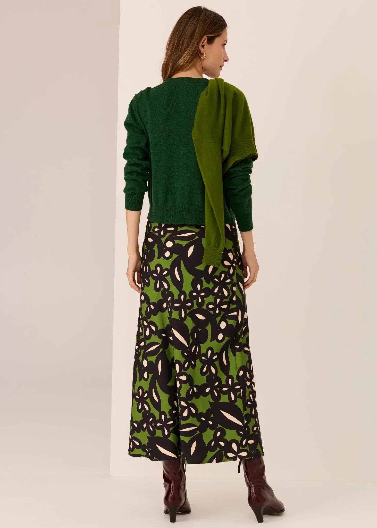 Woman in green floral midi skirt, matching sweater, and burgundy boots, back view