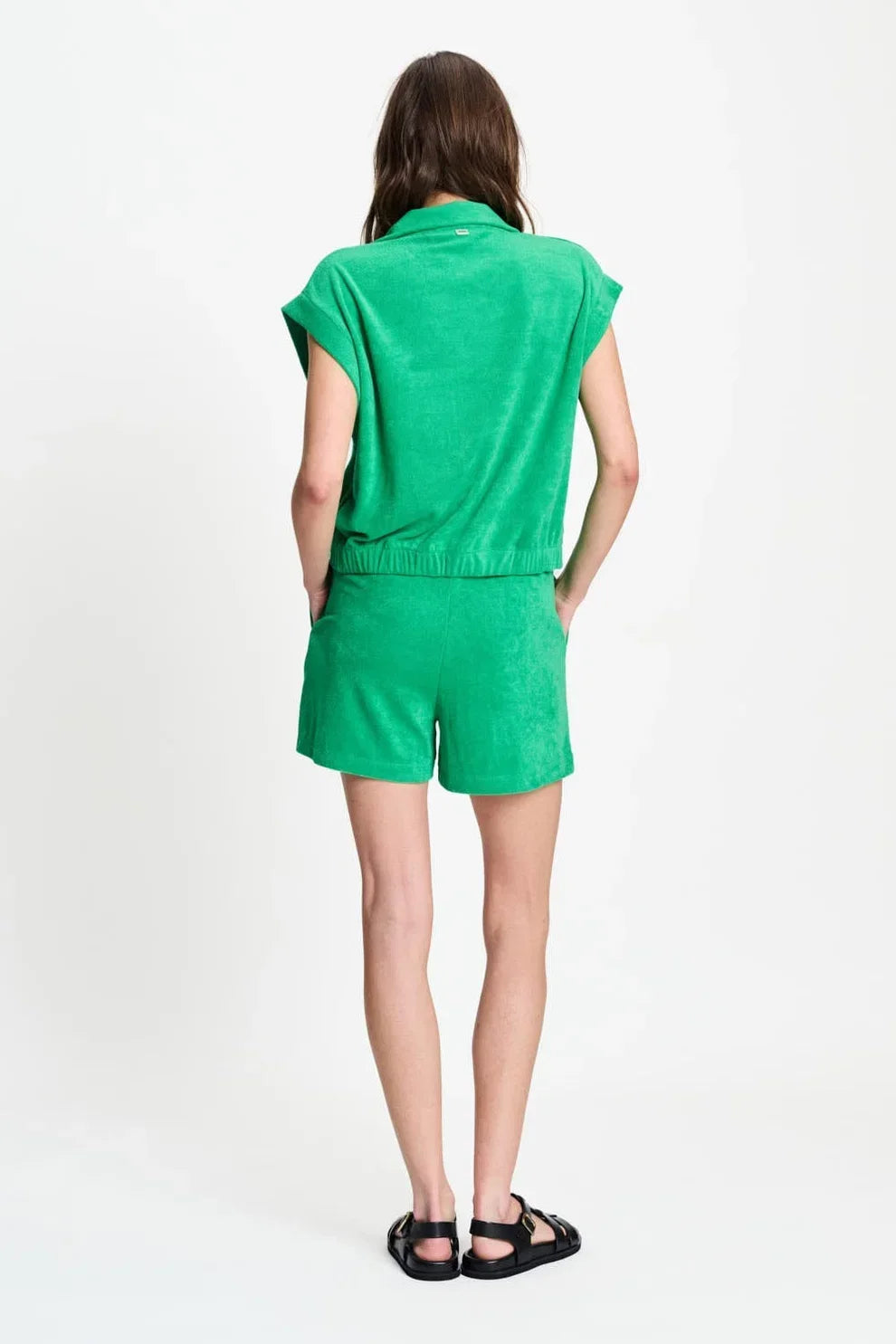 Woman wearing a vibrant green short-sleeved knit top and matching shorts with black sandals.