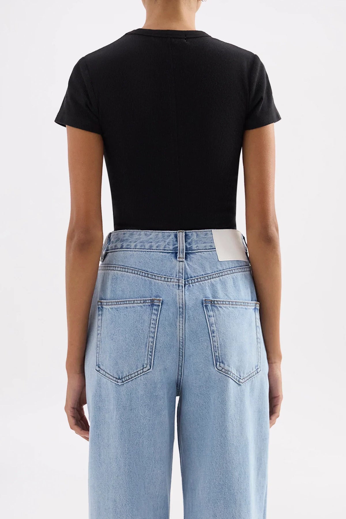 Back view of Nude Lucy Organic Rib SS Tee in black paired with light wash blue jeans.