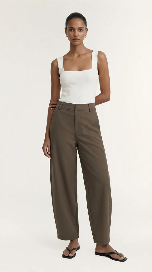 Woman wearing a white ribbed tank top and brown wide-leg trousers.