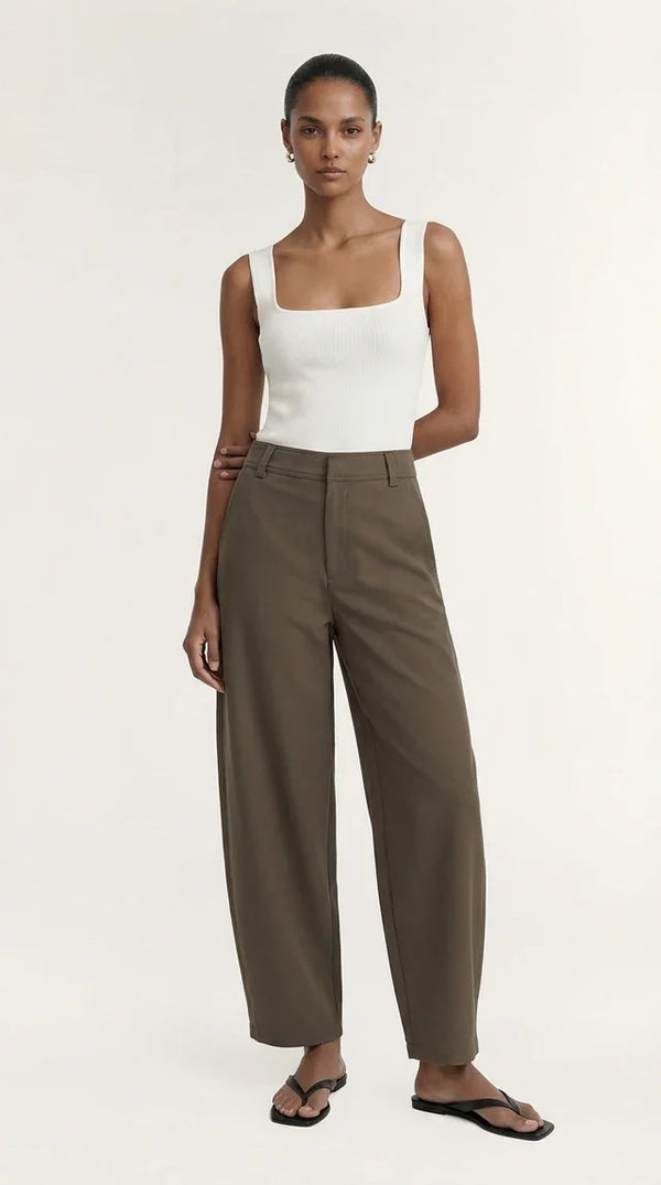 Woman wearing a white ribbed tank top and brown wide-leg trousers.