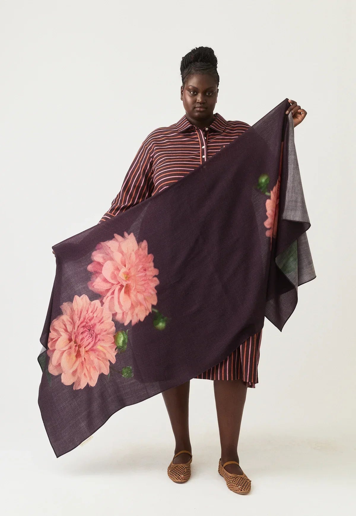 Woman modeling a large dark floral scarf with pink flowers, wearing a striped dress.