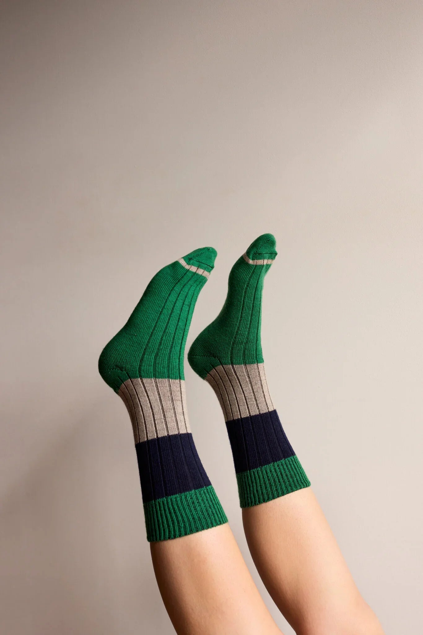 Person wearing green, navy, and beige colorblock ribbed socks against a neutral background