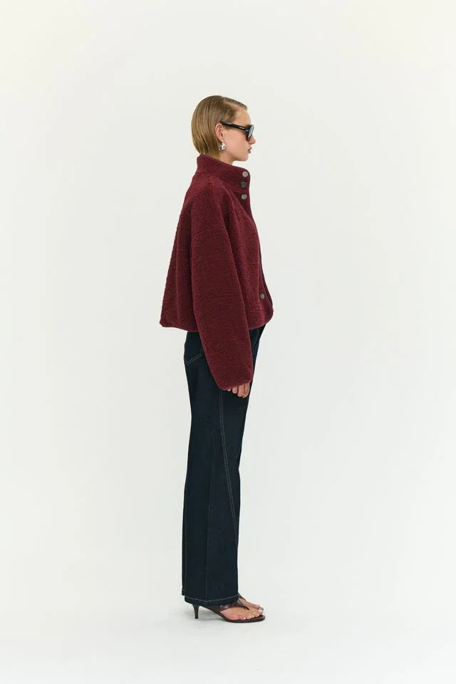 Woman in burgundy cropped teddy coat, dark jeans, and heeled sandals, side profile
