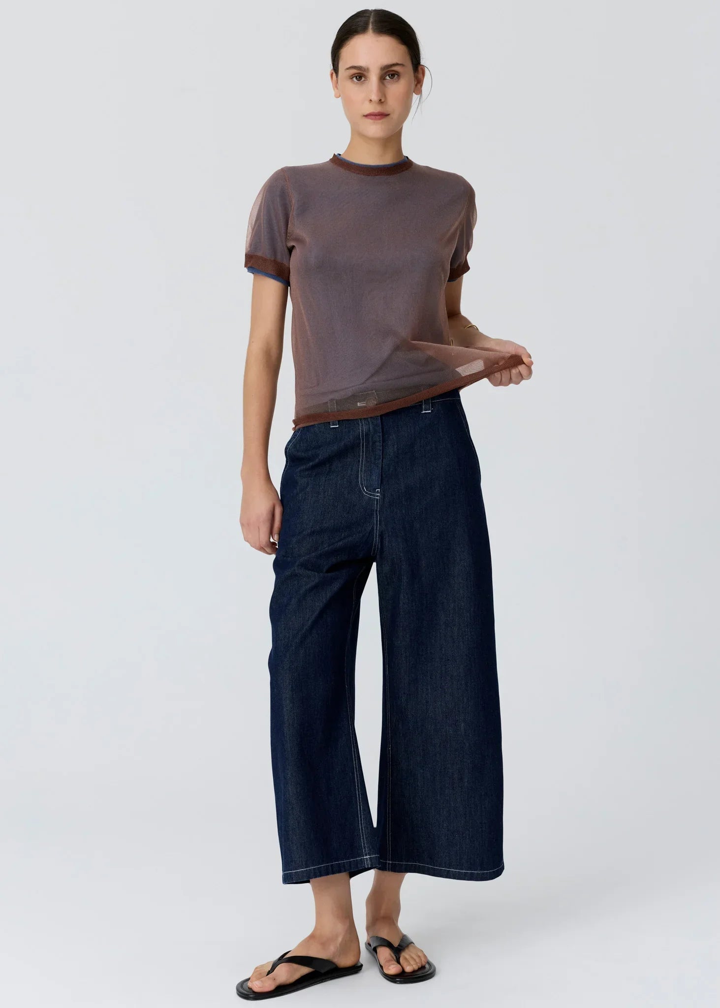 Woman wearing a sheer brown short-sleeve top and wide-leg dark wash denim jeans.