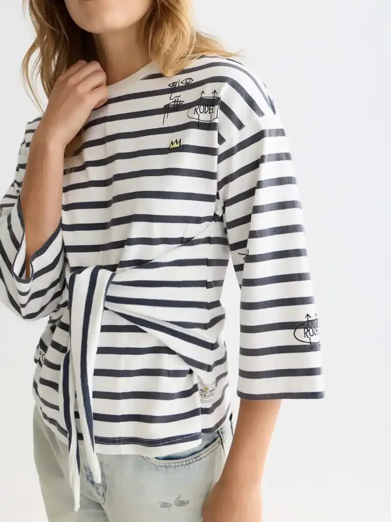 Striped women's top with tie front and graphic details, paired with light denim jeans